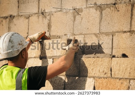 Bricklayer constructing stone wall using stone blocks, cement mortar mix and trowe