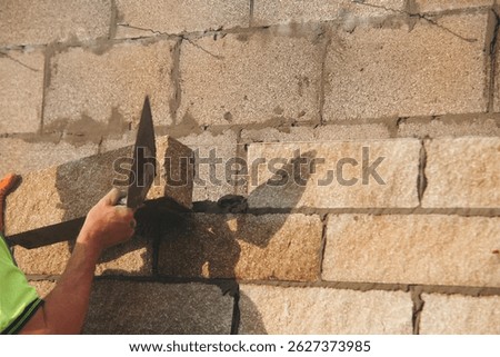 Bricklayer constructing stone wall using stone blocks, cement mortar mix and trowe