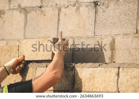 Bricklayer constructing stone wall using stone blocks, cement mortar mix and trowe