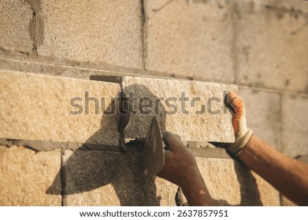 Bricklayer constructing stone wall using stone blocks, cement mortar mix and trowe
