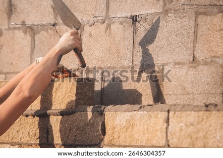 Bricklayer constructing stone wall using stone blocks, cement mortar mix and trowe
