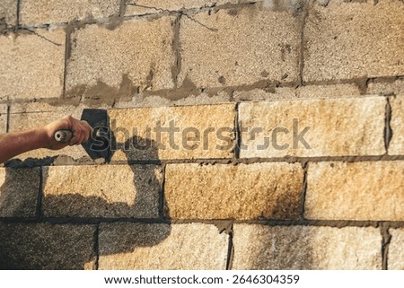 Bricklayer constructing stone wall using stone blocks, cement mortar mix and trowe