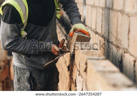 Bricklayer constructing stone wall using stone blocks, cement mortar mix and trowel