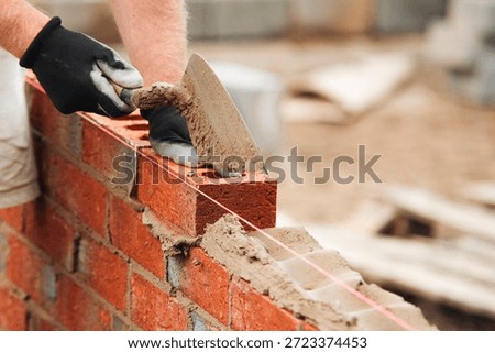 Bricklayer constructing stone wall using stone blocks, cement mortar mix and trowel