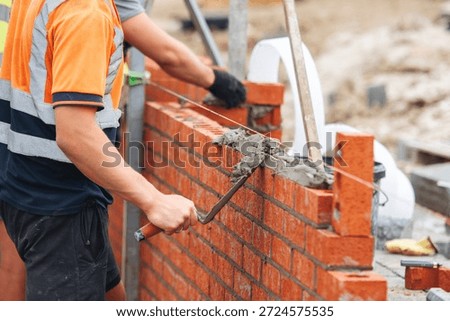Bricklayer constructing stone wall using stone blocks, cement mortar mix and trowel