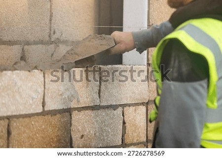 Bricklayer constructing stone wall using stone blocks, cement mortar mix and trowel