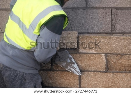 Bricklayer constructing stone wall using stone blocks, cement mortar mix and trowel