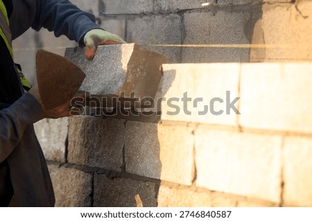 Bricklayer constructing stone wall using stone blocks, cement mortar mix and trowel