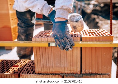 Bricklayer industrial worker installing brick masonry on exterior wall using level and rubber hammer