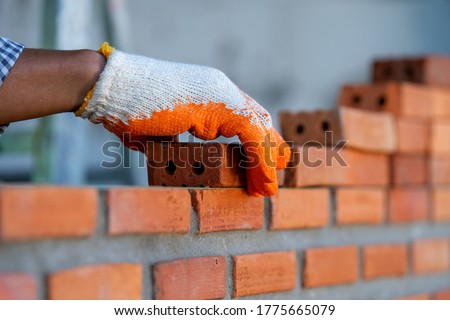 Bricklayer industrial worker installing brick masonry on exterior wall at new house.