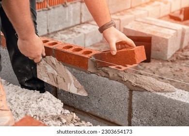 Bricklayer laying brick on cement mix on construction site close-up. Reduce the housing crisis by building more affordable houses concept - Shutterstock ID 2303654173