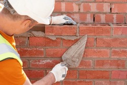 Bricklayer Laying Bricks On Mortar On New Residential House Construction. Get NVQ In Bricklaying