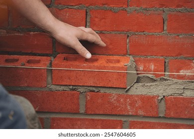 Bricklayer laying red bricks in a wall construction project on a sunny day with careful attention to detail - Powered by Shutterstock