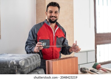 Bricklayer with measuring tape smiles looking at camera ready to cut a brick