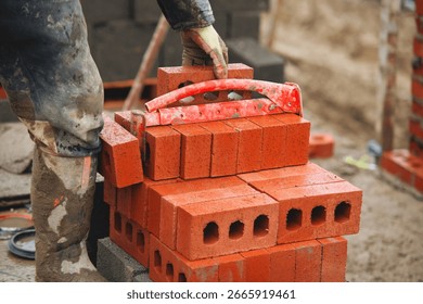 Bricklayer moving and stacking red bricks at busy building using brick tongs lifting carrier, showcasing dedication to craftsmanship and urban development