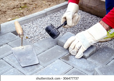 Bricklayer Places Concrete Paving Stone Blocks For Building Up A Patio, Using Hammer And Spirit Level