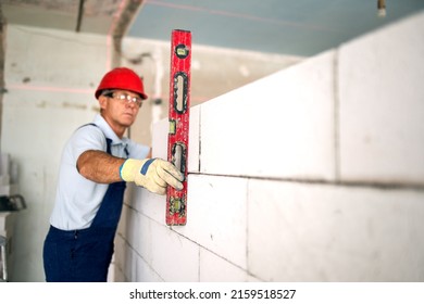 Bricklayer using spirit bubble and laser level to precise check concrete blocks on wall. Contractor uses tools for brickwork. Worker constructs a wall in new apartment real estate.