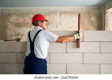 Bricklayer using spirit bubble and laser level to precise check concrete blocks on wall. Contractor uses tools for brickwork. Worker constructs a wall in new apartment real estate. - Powered by Shutterstock