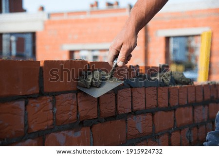 Bricklayer worker installing brick masonry on exterior wall. Professional construction worker laying bricks.