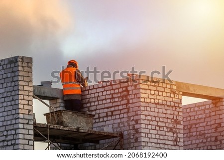 Bricklayer worker installing brick masonry on exterior wall. Professional construction worker laying bricks.