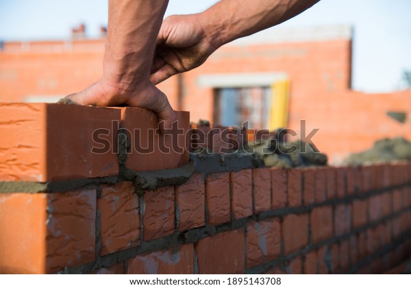 Bricklayer worker\
installing brick masonry on exterior wall. Professional\
construction worker laying\
bricks.
