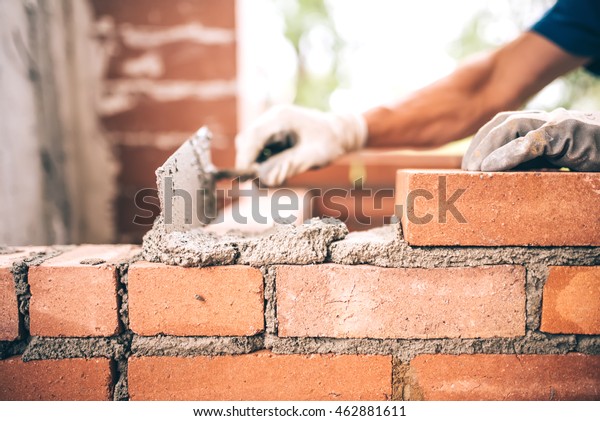 Bricklayer worker installing brick masonry on\
exterior wall with trowel putty\
knife