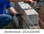 A bricklayer works on blocks to build a wall on a construction site with concrete, a trowel, a level and a grinder