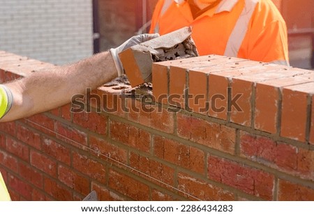 Bricklayers laying bricks on mortar Bricklayer making finishing touches to the brick wall and filling joints with mortar