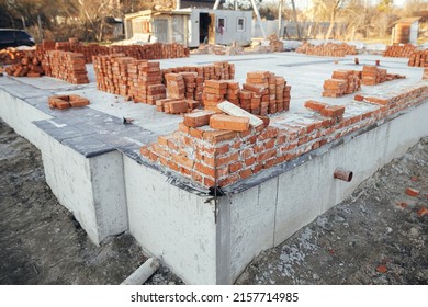 Bricks Masonry With Cement On Concrete Foundation, Process Of House Building. Red Bricks For Laying On Concrete Foundation. Building Materials At Construction Site