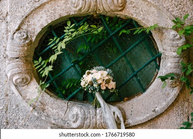 Bridal Bouquet Of White Roses, Eucalyptus Tree Branches, Sempervivum, Scabiosa And Blue Ribbons On The Oval Window Of An Ancient House