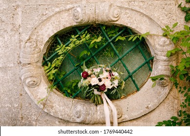 Bridal Bouquet Of White Roses, Eucalyptus Tree Branches, Helichrisum And White Ribbons On The Oval Window Of An Ancient House