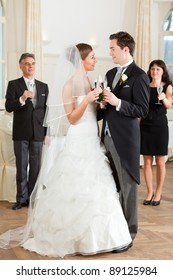 Bridal couple clinking glasses while the guests standing in the background