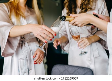 Bridal morning with bridesmaids drinking champagne, wearing silk light pink robes. Girls at the pyjama party with champagne glasses.