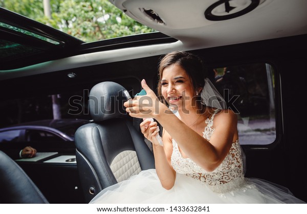 The bride adjusts her makeup\
in the back seat of the car. The girl paints her lips in the\
car.
