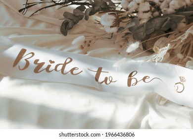 Bride To Be Golden And White Satin Sash Ribbon Accessory For A Bachelorette Party And Boho Neutral Dried Flowers On The Background