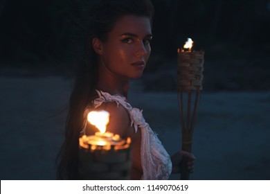 Bride in beautiful wedding dress is holding torchlight on the beach at night