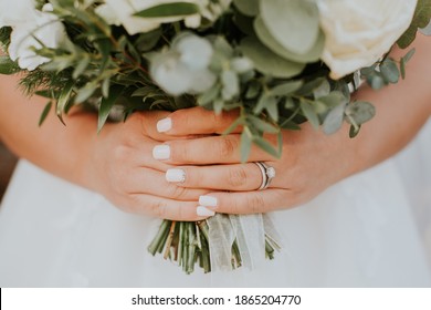
Bride in beautiful white wedding dress holding her wedding bouquet made from white and green flowers. Wearing  Detail of bride hands holding a beautiful wedding bouquet. Diamond wedding ring on hand.