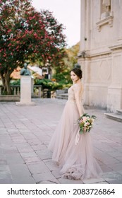 Bride With A Bouquet Of Flowers Stands Near An Ancient Building In The Garden