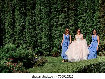 Bride and bridesmaids in blue dresses walk in a green garden - Shutterstock ID 736910518
