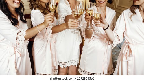 Bride And Bridesmaids Stand In Silk Robes With Glasses Of Champagne