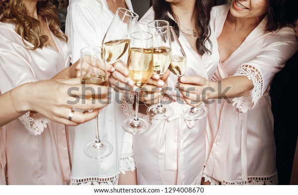 Bride and bridesmaids stand in silk robes with\
glasses of champagne
