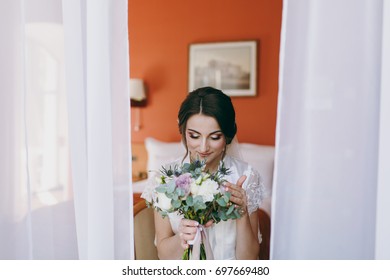 The Bride Brunette In Veil And White Satin Dressing Gown Sits By The Window