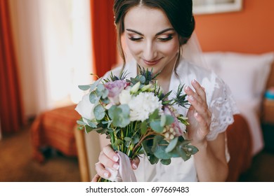 The Bride Brunette In Veil And White Satin Dressing Gown Sits By The Window