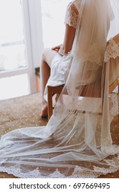 The Bride Brunette In Veil And White Satin Dressing Gown Sits By The Window