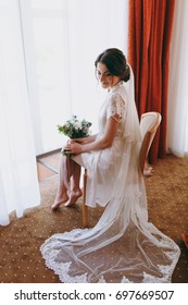 The Bride Brunette In Veil And White Satin Dressing Gown Sits By The Window