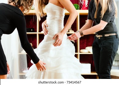 Bride At The Clothes Shop For Wedding Dresses; She Is Choosing A Dress And The Designer Are Assisting Her