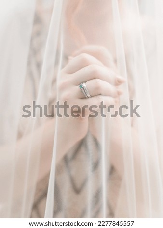 The bride, covered in a white veil, folded her arms. Wedding ring on the bride's hand, a ring with an emerald. Bride's hands.