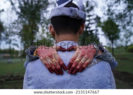 The bride is doing heart shape with her hands at the back of the groom.