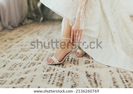 Bride dresses shoes before the wedding ceremony. Closeup detail of bride putting on high heeled sandal wedding shoes.