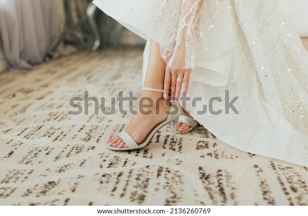Bride\
dresses shoes before the wedding ceremony. Closeup detail of bride\
putting on high heeled sandal wedding\
shoes.
